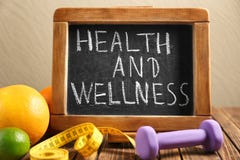 Phrase \"Health and wellness\" written on blackboard, fruits and dumbbell on wooden table