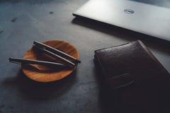 Piattino del caffè, penne di lusso, computer portatile e taccuino sulla tavola concreta fotografia stock libera da diritti Piattino del caffè, penne di lusso, computer portatile e taccuino sulla tavola concreta fotografia stock libera da diritti