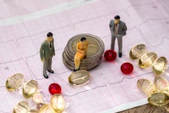 Piccolo gioca la gente per trovare sulle euro monete e sul cardiogramma fra le pillole fotografia stock Piccolo gioca la gente per trovare sulle euro monete e sul cardiogramma fra le pillole fotografia stock