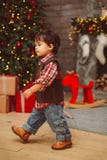 Piccolo ragazzo alla moda che cammina vicino all'albero di Natale fotografia stock libera da diritti Piccolo ragazzo alla moda che cammina vicino all'albero di Natale fotografia stock libera da diritti
