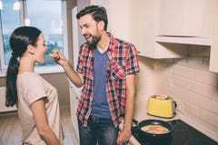 Pictue precioso del hombre que se coloca delante de mujer y que sostiene la cuchara de madera con el pedazo de omlet Ella lo mira fotografía de archivo Pictue precioso del hombre que se coloca delante de mujer y que sostiene la cuchara de madera con el pedazo de omlet Ella lo mira fotografía de archivo
