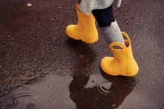 Pies del niño en las botas de goma amarillas que saltan sobre un charco en th imagenes de archivo Pies del niño en las botas de goma amarillas que saltan sobre un charco en th imagenes de archivo
