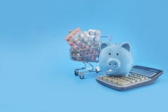 Piggy bank and basket with pills on a blue background, concept of saving on drugs, online shopping