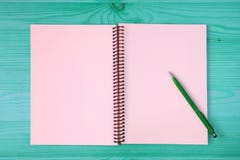 Pink blank page of an opened notebook and a green pen on the blue green wooden table royalty free stock photography Pink blank page of an opened notebook and a green pen on the blue green wooden table royalty free stock photography