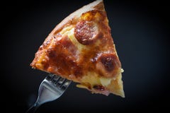 Pizza on fork / Slice pizza piece on the dark black stock photo Pizza on fork / Slice pizza piece on the dark black stock photo