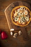 Pizza med den kyliga pepparchampinjonen med den bruna lantliga tabellen arkivbild Pizza med den kyliga pepparchampinjonen med den bruna lantliga tabellen arkivbild