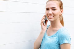 Piękna dziewczyna opowiada na telefonie na drewnianym białym tle, szeroki uśmiech obraz stock Piękna dziewczyna opowiada na telefonie na drewnianym białym tle, szeroki uśmiech obraz stock