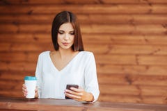 Piękna młoda kobieta używa jej smartphone i pijący kawę obraz stock Piękna młoda kobieta używa jej smartphone i pijący kawę obraz stock