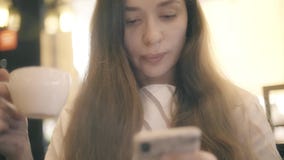 Piękna młoda kobieta używa jej smartphone podczas gdy mieć herbaty lub kawy w kawiarni zbiory wideo Piękna młoda kobieta używa jej smartphone podczas gdy mieć herbaty lub kawy w kawiarni zbiory wideo
