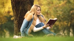 Pięknej kobiety czytelniczy bestseller jako obsiadanie pod drzewem w jesień lesie, hobby fotografia stock Pięknej kobiety czytelniczy bestseller jako obsiadanie pod drzewem w jesień lesie, hobby fotografia stock