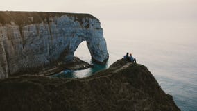 Piękny tylny widok szczęśliwy mężczyzna i kobieta siedzi blisko siebie oglądający zmierzchu ocean na górze Normandy wybrzeża fale zbiory Piękny tylny widok szczęśliwy mężczyzna i kobieta siedzi blisko siebie oglądający zmierzchu ocean na górze Normandy wybrzeża fale zbiory