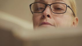 Plan rapproché d'une femme poussant des feuilles par un livre Blonde avec des verres lisant un livre clips vidéos Plan rapproché d'une femme poussant des feuilles par un livre Blonde avec des verres lisant un livre clips vidéos