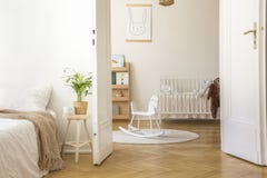 Planta no tamborete ao lado da cama no interior branco do quarto com o cavalo de balanço no tapete e no berço fotografia de stock royalty free Planta no tamborete ao lado da cama no interior branco do quarto com o cavalo de balanço no tapete e no berço fotografia de stock royalty free