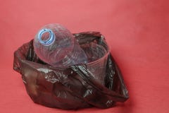 Plastic empty bottle in a black bag in container on red background. Concept of environmental pollution by plastic trash stock photography Plastic empty bottle in a black bag in container on red background. Concept of environmental pollution by plastic trash stock photography