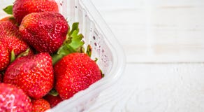 Plastic tray with red strawberries on a white wooden background stock images Plastic tray with red strawberries on a white wooden background stock images