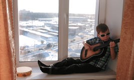 Playing a musical instrument. Boy in sunglasses plays the guitar sitting on the windowsill. stock images Playing a musical instrument. Boy in sunglasses plays the guitar sitting on the windowsill. stock images