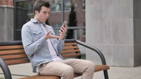 Plenerowy młody człowiek niepokojący stratą podczas gdy używać smartphone zdjęcie wideo Plenerowy młody człowiek niepokojący stratą podczas gdy używać smartphone zdjęcie wideo
