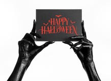 Pocztówkowy i Szczęśliwy Halloweenowy temat: czarna ręka trzyma papierową kartę z słowami Szczęśliwy Halloween na śmierć biali od fotografia stock Pocztówkowy i Szczęśliwy Halloweenowy temat: czarna ręka trzyma papierową kartę z słowami Szczęśliwy Halloween na śmierć biali od fotografia stock