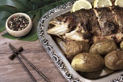 Poissons grillés avec des pommes de terre et tranches de citron d'un plat argenté avec les bâtons et les épices en bois asiatique image stock Poissons grillés avec des pommes de terre et tranches de citron d'un plat argenté avec les bâtons et les épices en bois asiatique image stock