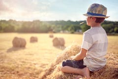 Pojkesammanträde på en höstack i sommar som håller ögonen på solnedgången Arkivfoton Pojkesammanträde på en höstack i sommar som håller ögonen på solnedgången Arkivfoton
