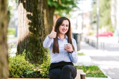 Pollici su dalla giovane bella donna di affari che utilizzano il cellulare all'aperto fotografia stock libera da diritti Pollici su dalla giovane bella donna di affari che utilizzano il cellulare all'aperto fotografia stock libera da diritti