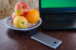 Pommes et oranges d'un plat à côté d'un ordinateur portable, téléphone intelligent sur la table Image stock Pommes et oranges d'un plat à côté d'un ordinateur portable, téléphone intelligent sur la table Image stock