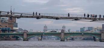 Ponte di millennio in priorità alta con i pedoni che camminano attraverso Nel ponte di Southwark di distanza ed oltre quel ponte immagini stock libere da diritti Ponte di millennio in priorità alta con i pedoni che camminano attraverso Nel ponte di Southwark di distanza ed oltre quel ponte immagini stock libere da diritti