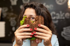 Portrai de la jeune femme caucasienne de brune regardant par le sandwich mordu images stock Portrai de la jeune femme caucasienne de brune regardant par le sandwich mordu images stock