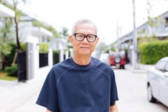 Portrait of Asian senior man wearing glasses and looking at camera in the residential district with car and house in background. Stock Image Portrait of Asian senior man wearing glasses and looking at camera in the residential district with car and house in background. Stock Image