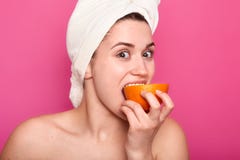 Portrait of attractive woman with nacked shoulders, girl eats orange and looks at camera. Charming female with towel on head has stock photography Portrait of attractive woman with nacked shoulders, girl eats orange and looks at camera. Charming female with towel on head has stock photography
