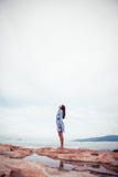 A portrait of beautiful asian woman in dress stand on a stone by the sea and looks up