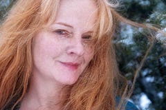 Portrait of a beautiful red-haired woman in the best age with snowflakes in hair with shawl, is leaning against a tree and happily stock photo Portrait of a beautiful red-haired woman in the best age with snowflakes in hair with shawl, is leaning against a tree and happily stock photo