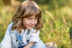 A portrait of a cute little boy with blue eyes and long blond hair sitting on a basket outside at sunset royalty free stock photography A portrait of a cute little boy with blue eyes and long blond hair sitting on a basket outside at sunset royalty free stock photography