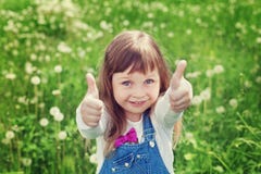 Portrait of cute little girl with thumbs up shows a class on the flower meadow, happy childhood concept, child having fun