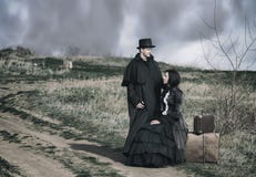 Portrait d'ext?rieur d'une dame victorian dans la s?ance noire sur la route avec son bagage et monsieur se tenant tout pr?s image stock Portrait d'ext?rieur d'une dame victorian dans la s?ance noire sur la route avec son bagage et monsieur se tenant tout pr?s image stock