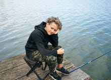 Portrait d'une pêche d'adolescent sur la banque de la rivière ou du lac Garçon mignon avec les cheveux bouclés photos libres de droits Portrait d'une pêche d'adolescent sur la banque de la rivière ou du lac Garçon mignon avec les cheveux bouclés photos libres de droits