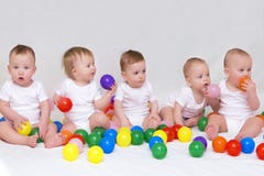 Portrait de cinq bébés mignons sur le fond clair jouant avec les boules colorées images stock Portrait de cinq bébés mignons sur le fond clair jouant avec les boules colorées images stock