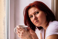 Portrait de femme tenant la tasse blanche de café près de la fenêtre et regardant la caméra La femelle a soumis à une contrainte photo libre de droits Portrait de femme tenant la tasse blanche de café près de la fenêtre et regardant la caméra La femelle a soumis à une contrainte photo libre de droits