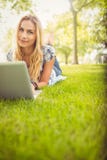 Portrait de la femme de sourire à l'aide de l'ordinateur portable tout en se trouvant sur l'herbe Photographie stock libre de droits