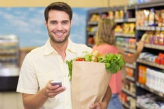 Portrait des produits alimentaires et d'à l'aide de achat de sourire d'homme bel de son smartphone photos stock Portrait des produits alimentaires et d'à l'aide de achat de sourire d'homme bel de son smartphone photos stock