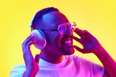 Portrait of e African-American man emotionally listening to music in headphones and singing against yellow studio