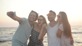 Portrait of Four Friends Taking Selfie Using Smartphone Together on the Seaside during Windy Weather. stock footage Portrait of Four Friends Taking Selfie Using Smartphone Together on the Seaside during Windy Weather. stock footage