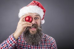 Portrait of a funny bearded man wearing santa cap and holding a. Red round Christmas ball over gray background Stock Photography Portrait of a funny bearded man wearing santa cap and holding a. Red round Christmas ball over gray background Stock Photography