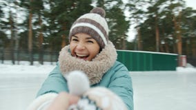Portrait of happy young woman in warm clothes ice-skating laughing looking at camera