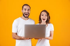 Portrait of lovely man and woman holding silver laptop, while standing isolated over yellow background royalty free stock images Portrait of lovely man and woman holding silver laptop, while standing isolated over yellow background royalty free stock images