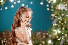 Portrait Of A Smiling Long-haired Little Girl In Dress On Background Of Christmas Lights. Little Girl Talking On The Phone. Stock Photo