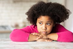 Portrait Of Cute Sad Little Black Girl Sitting At Table In Kitchen. Royalty Free Stock Image