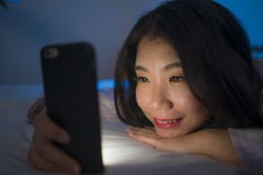 Portrait Of Young Beautiful And Happy Sweet Asian Korean Woman With In Pajamas Enjoying With Mobile Phone App In Bed At Night Stock Image