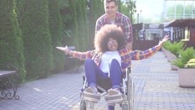 Portrait of a positive smiling young African American woman disabled in a wheelchair and her friend rejoices and raises stock video footage Portrait of a positive smiling young African American woman disabled in a wheelchair and her friend rejoices and raises stock video footage