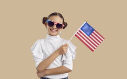 Portrait of pretty girl in sunglasses standing in studio, holding American flag and smiling